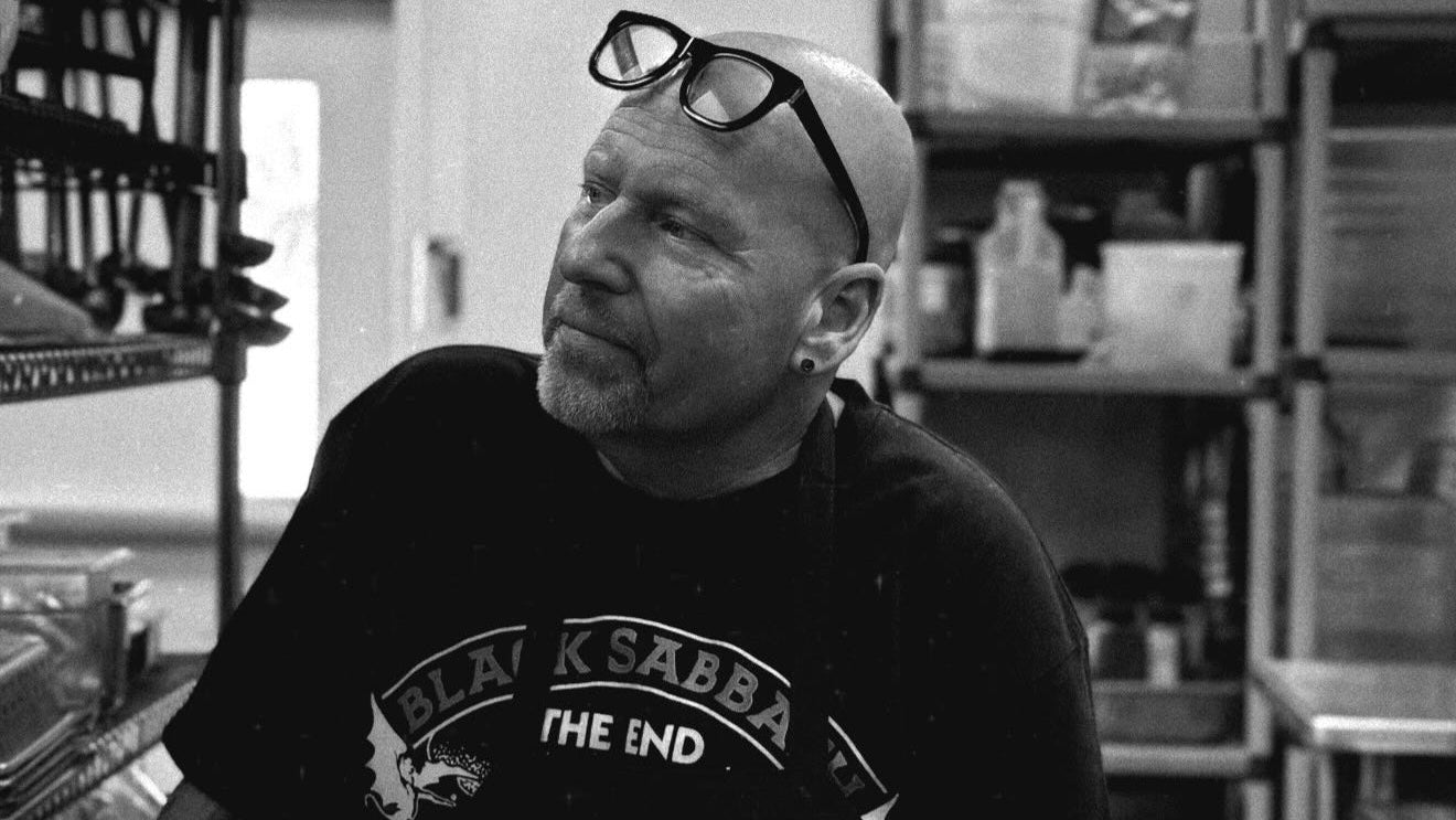 Person wearing a Black Sabbath t-shirt with a bald head and glasses, sitting in a room.